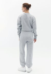 Grå cropped sweatshirt og matchende joggers lavet af blødt, tekstureret stof. Har ribbede manchetter og elastisk talje; båret med hvide sneakers.