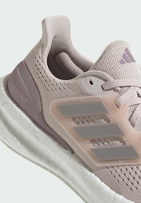 Close-up of light pink Adidas PureBoost running shoe with mesh upper, cushioned white sole, and three grey stripes on the side.