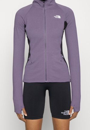 Veste à fermeture éclair violette avec passages pour les pouces et shorts de cycliste noirs, tous deux arborant le logo The North Face à l'avant.