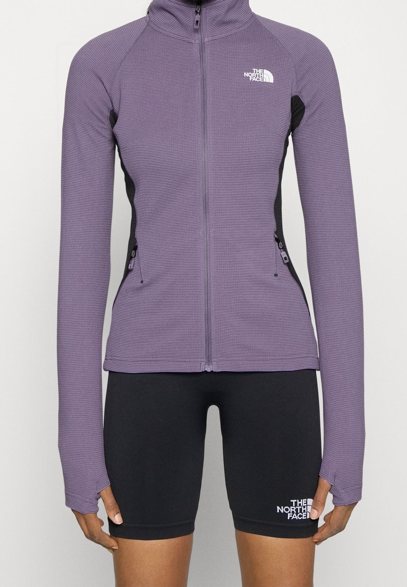 Veste à fermeture éclair violette avec passages pour les pouces et shorts de cycliste noirs, tous deux arborant le logo The North Face à l'avant.