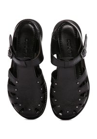 Sandali neri in pelle con cinturino alla caviglia regolabile, design open-toe, dettagli a taglio e piccoli chiodini decorativi lungo i bordi.