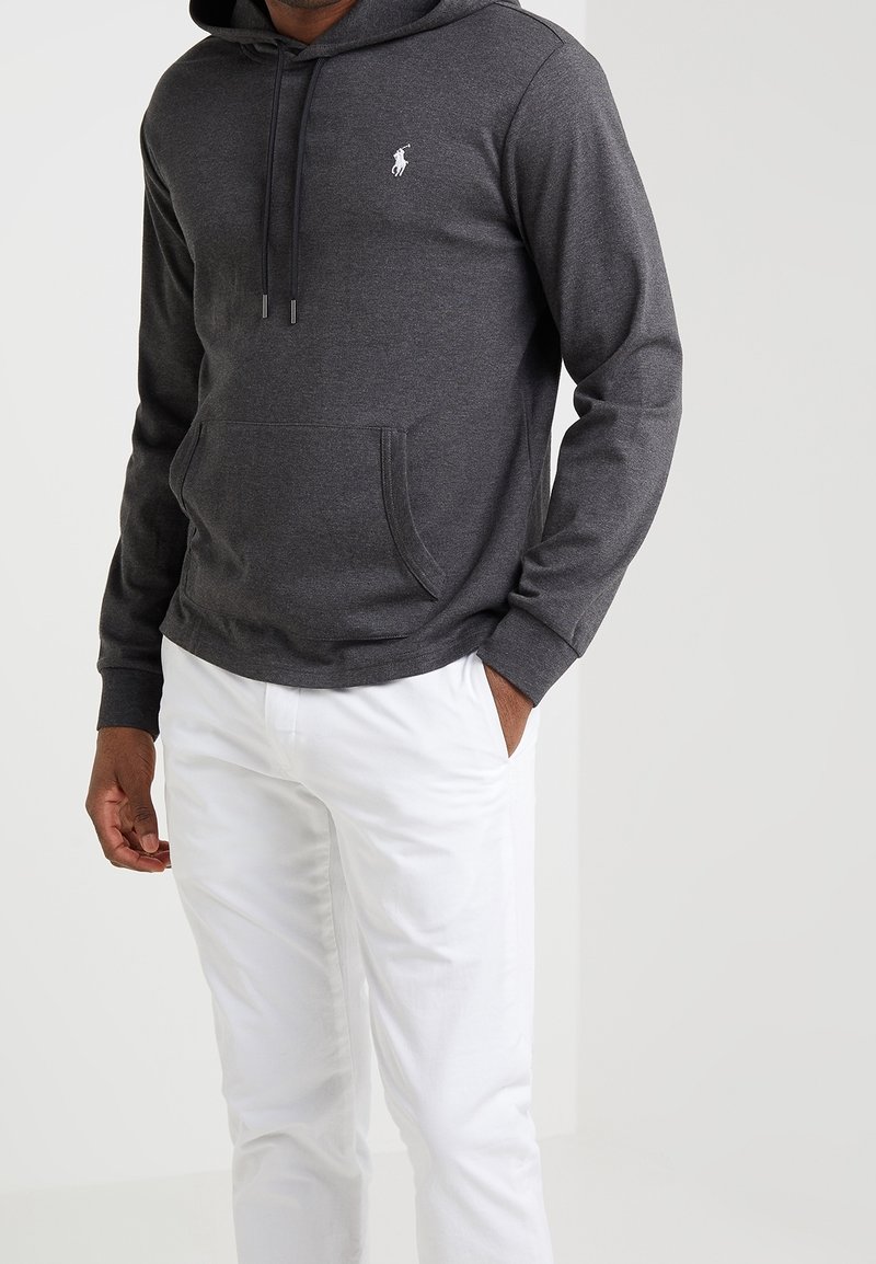 Grijze hoodie van zachte stof met een buidelzak aan de voorkant en een capuchon met trekkoord. Heeft een klein wit logo op de borst. Draag het met witte broek.