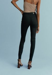 Jeans noirs taille haute avec une coupe ajustée, dotés de poches arrière et d'une longueur chevillée, associés à des sandales à talons à motifs.