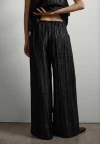 Pantalones de pierna ancha negros, hechos de tejido acanalado y texturizado; cinturilla elástica; combinados con una blusa holgada que muestra una silueta casual.