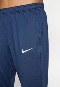 Navyträningbyxor med elastisk midja, sidoficka, med en vit Nike swoosh-logotyp. Tillverkade av lätt, slät tyg.