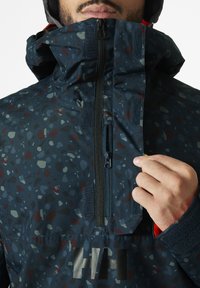 Granatowa wodoodporna kurtka z kolorowym nakropionym wzorem, wysoki kołnierz, zamek błyskawiczny z przodu oraz rzepy przy mankietach. Posiada logo na dolnej części przodu.