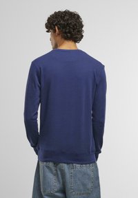 Dark blue long-sleeve sweatshirt with ribbed cuffs and hem, featuring a crew neck and a smooth texture on the fabric. Back view of the garment.