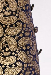 Teren de țesătură bleumarin cu un model paisley aurit, având o suprafață texturată și accente decorative sub formă de nasturi. Vedere de aproape.