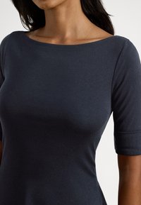 Tamno mornarsko plava pripijena majica napravljena od rastezljivog pamuka s okruglim izrezom i kratkim rukavima, karakterizirana glatkom teksturom i jednostavnim dizajnom.