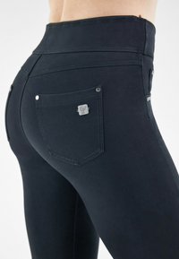 Mustat korkeavyötäröiset farkut, joissa on sileä kankaan rakenne, huomaamaton ommel, kaksi takataskua ja pieni metallinen logo-akkentti yksiin taskuista.