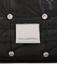 Mustahiili nahkapussi, jossa on hopeanvärisiä yksityiskohtia, kuten koristeellisia niittejä ja suorakulmainen logo-plaaketti, johon on kaiverrettu "KARL LAGERFELD."