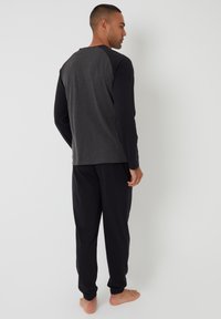 Conjunto de pijama de dos tonos de manga larga que presenta una parte superior gris oscuro con mangas negras y pantalones negros con cintura elástica. Tejido suave con un ajuste relajado.
