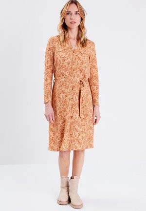 Langärmliges, knopfbares Kleid in Orange mit floralem Muster, an der Taille mit einem Gürtel gerafft. Ergänzt durch beigen Knöchelstiefel.