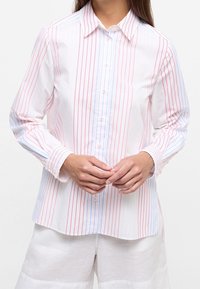 Camisa blanca de manga larga con franjas verticales rojas y azules, con botones en la parte delantera y cuello puntiagudo. Tejido suave con una textura lisa.