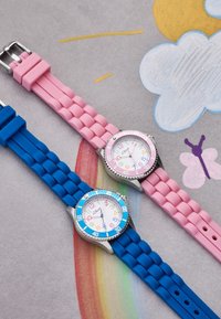 Zwei Uhren mit Silikonarmband: eine blaue mit einem silbernen Gehäuse und weißem Zifferblatt, die andere pink mit einem ähnlichen Design und bunten Minutenmarkierungen.