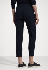 Marineblauwe high-waisted tapered broek met een gladde textuur, gecombineerd met zwarte leren sneakers met een beige zool en subtiele merkaccenten.