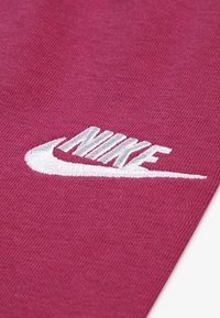 Bordová tkanina s textúrovaným povrchom, so vyšitým bielym logom Nike a charakteristickým dizajnom swoosh.