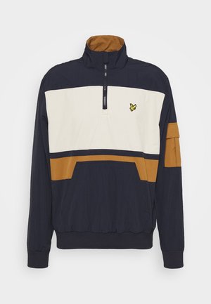 Chaqueta tipo pulóver de color azul marino, blanco y marrón con media cremallera, cuello alto, bolsillo frontal y un pequeño logotipo de pájaro amarillo en el pecho.