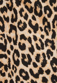Tkanina s leopardím vzorem s béžovým pozadím a velkými černými skvrnami, prezentující strukturovaný pletený materiál.