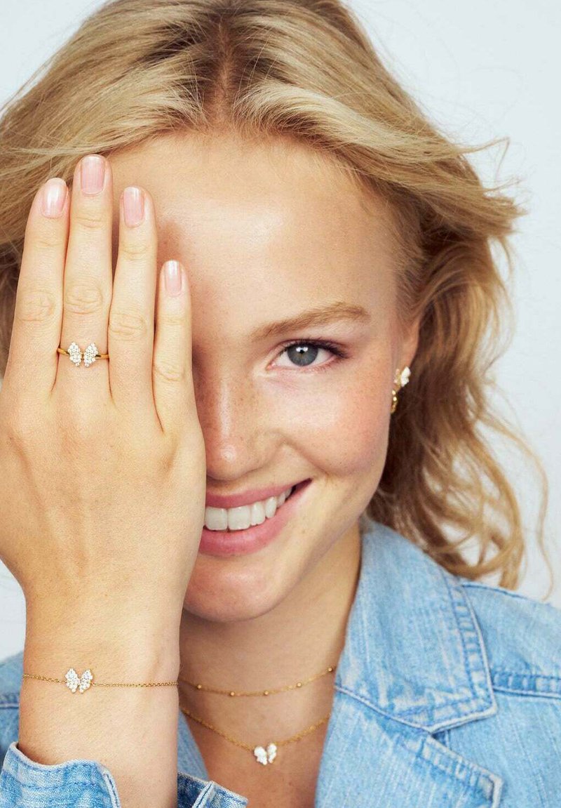 Guld fjädrande smycken, som inkluderar en ring och armband med klara ädelstenar, mot en bakgrund av lätt denimjacka.