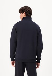 Felpa blu navy con colletto alto, polsini e orlo a coste. Realizzata in un tessuto liscio e morbido. Presenta una vestibilità comoda.