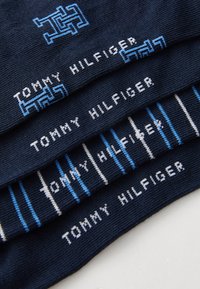 Dunkelblaue Socken mit wiederholtem "TOMMY HILFIGER"-Text in Weiß und Hellblau, wobei ein Paar ein geometrisches Design und die anderen gestreifte Muster aufweisen.