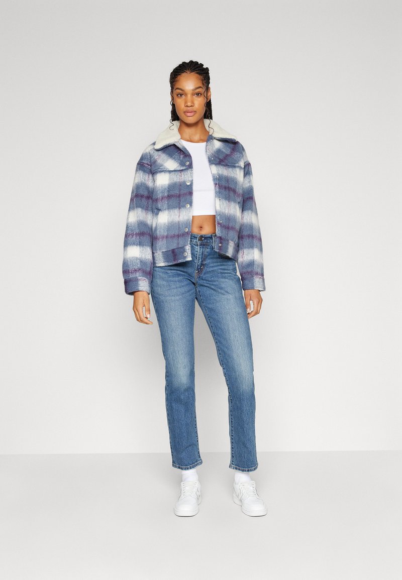 Veste à carreaux coupée dans des tons de bleu et de blanc, avec un col en fausse fourrure, associée à un jean en denim clair et des baskets blanches.