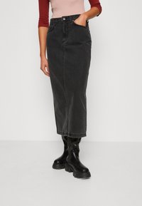 Črna denim midi krila z ravnim krojem, sprednjimi žepi in vidnim šivanjem. Ustrezno v kombinaciji z črnimi škornji do kolen.