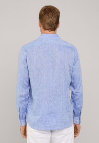 Lichtblauw langemouwen shirt van een gestructureerde stof, met een button-down kraag en knopenmanchetten. Heeft een achterpand en zijopeningen voor ventilatie.