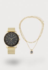 Montre avec un bracelet en maille dorée, un cadran noir et des accents dorés ; accompagnée de deux colliers en chaîne dorée superposés avec un pendentif rectangulaire.
