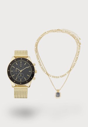 Montre avec un bracelet en maille dorée, un cadran noir et des accents dorés ; accompagnée de deux colliers en chaîne dorée superposés avec un pendentif rectangulaire.