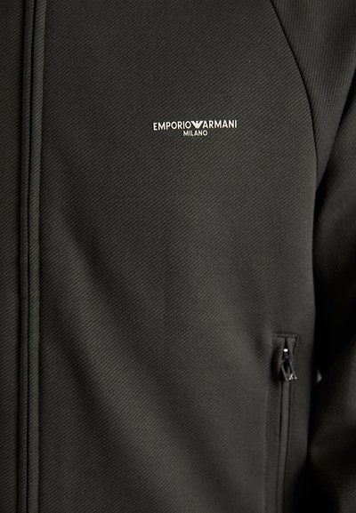 Čierna textúrovaná bunda s vreckom na zips a malým strieborným logom Emporio Armani. Tkanina má hladký, štruktúrovaný vzhľad.