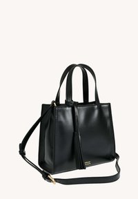 Sac à main en cuir noir avec double poignées, bandoulière détachable et détail de frange sur fond neutre.