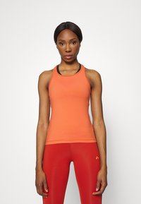 Top deportivo naranja con diseño de espalda nadadora, que presenta un ajuste ceñido y un ribete de color contrastante en el cuello, combinado con leggings rojos.