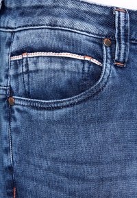 Tmavomodré džíny z denimu s klasickým dizajnom piatich vreciek, viditeľným stehom vo svetlom pomarančovom odtieni a kovovým detailom na gombíku.