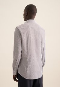 Camicia a maniche lunghe con tessuto a fantasia in bianco, blu navy e rosso. Collo standard, polsini con bottone, orlo curvo e vestibilità sagomata.
