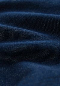 Tissu en denim bleu marine avec une texture lisse, présentant de subtiles variations dans le tissage et une légère brillance reflétant la lumière.