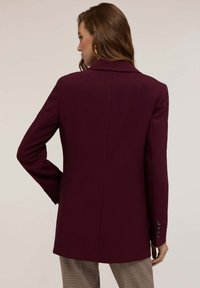 Bordeaux op maat gemaakte blazer met scherpe revers en lange mouwen, voorzien van knoopaccenten op de manchetten en een gladde, gestructureerde stof.