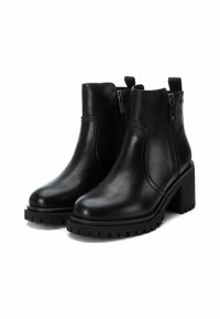 Botas negras de tobillo hechas de cuero con un tacón grueso y suela de goma, que cuentan con cremalleras laterales y tiradores para ponerlas y quitarlas fácilmente.