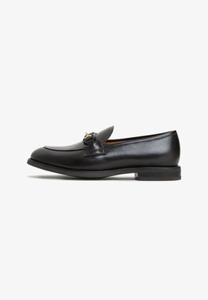 Mocassino in pelle nera con punta tonda, design sobrio e un accento in metallo dorato sulla parte anteriore. Suola in gomma piatta.