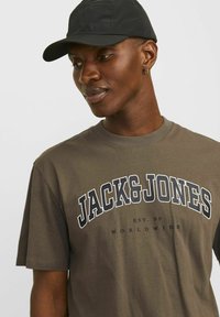 Oliven grøn bomulds t-shirt med fed hvid og sort tekst, der står "JACK & JONES", med rund hals og korte ærmer.