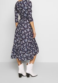 Robe florale bleu marine à manches trois-quarts, avec un ourlet froncé et une taille cintrée. Assortie à des bottes de cowboy blanches et à un talon bloc noir.