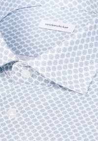 Chemise blanche à motifs géométriques bleus, col plié et boutons visibles, étiquetée "seidensticker".