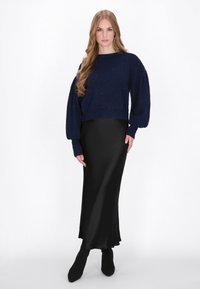 Marineblauw gebreid sweater met pofmouwtjes, versierd met subtiele sprankelingen, gecombineerd met een strakke zwarte satijnen maxi rok en zwarte enkellaarsjes.