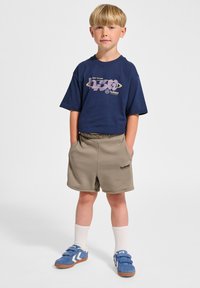 Marinblå t-shirt med grafiskt tryck, beige shorts med elastisk midja, blå sneakers med kardborreband och vita strumpor.