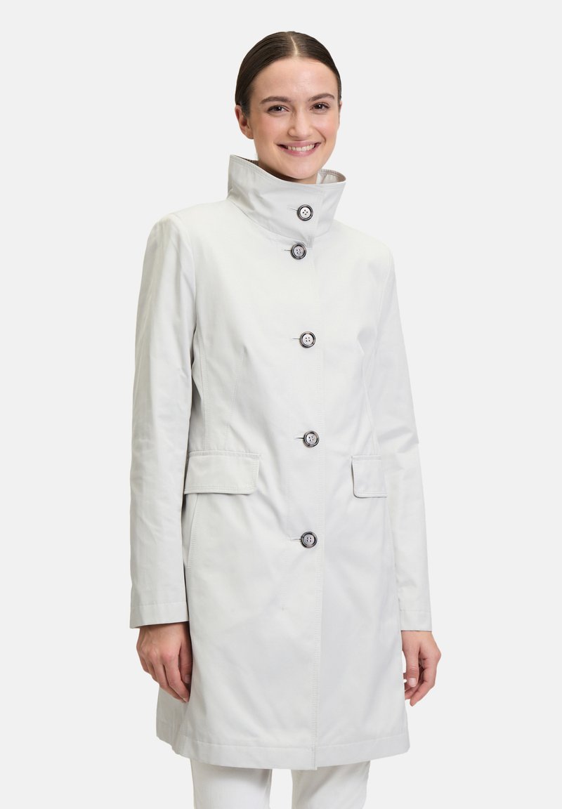 Lichtgrijs, knielang jasje met een hoge kraag, knoopsluiting aan de voorkant en twee zijzakken. Kenmerkt zich door een gladde stof en vijf decoratieve knopen.