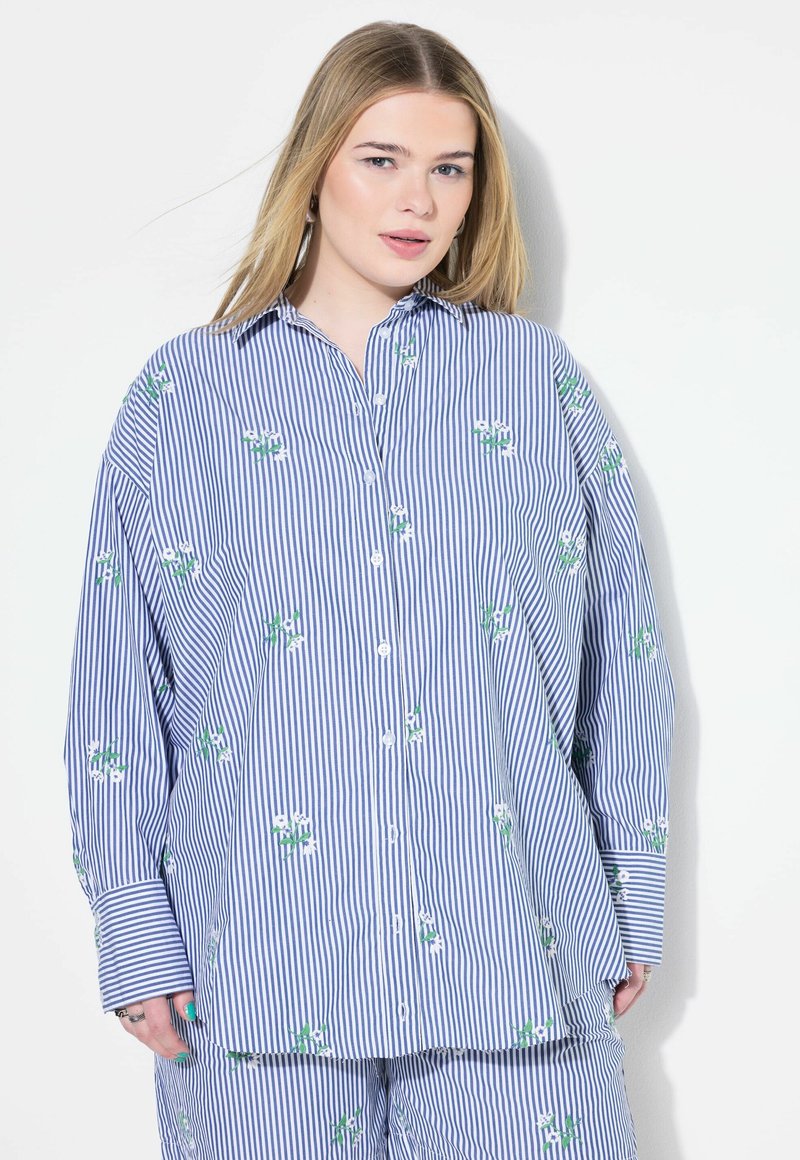 Camicia a righe blu e bianca con ricami floreali verdi. Dotata di una vestibilità ampia e maniche lunghe con polsini larghi.