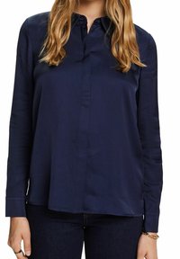 Mörkblå långärmad blus med krage, knappstängning framtill och en slät, något blank yta. Slutet är rakt och löst passande.