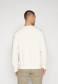 Sweatshirt alb cu guler rotund, cu mâneci lungi, manșete și talie ribbate, asortat cu pantaloni khaki deschis. Materialul pare moale și texturat.