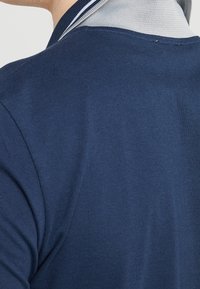 Camisa polo navy con tejido texturizado, con un cuello en contraste de gris claro. Diseño simple y limpio con un ajuste clásico.